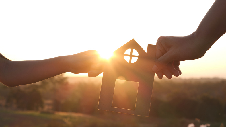  Mother and daughter hands holding paper house home together silhouette against sunset with soft focus Concept of Happy Family Buy House Home life insurance care saving mortgage estate